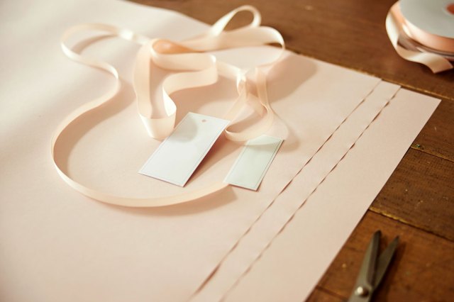 An image of cut satin ribbon piece and two blank gift tags lying on several sheets of flower packaging paper on a wooden table