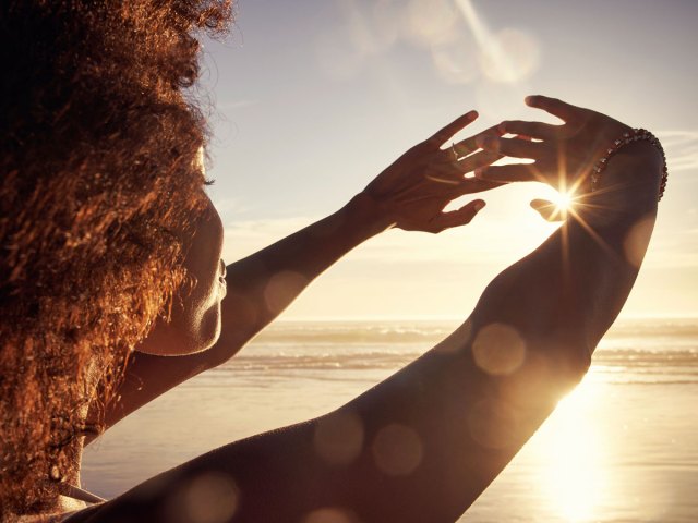 An image of a woman at the beach holding her hands up to the sun