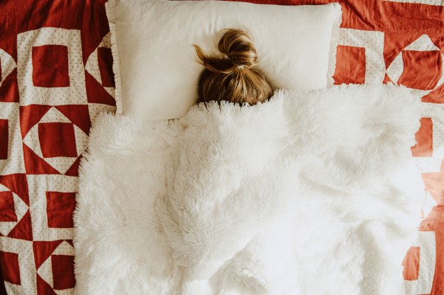 An image of a woman in bed with a white blanket over her head