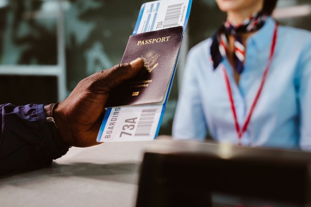 An image of a person holding a passport and boarding ticket at an airline desk