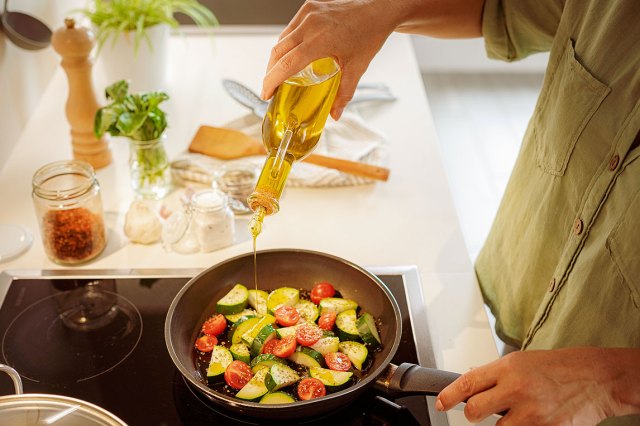 An image of a person pouring oil into a pan of vegetables