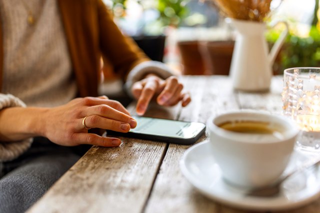 An image of a woman sitting at a coffee shop table on her phone
