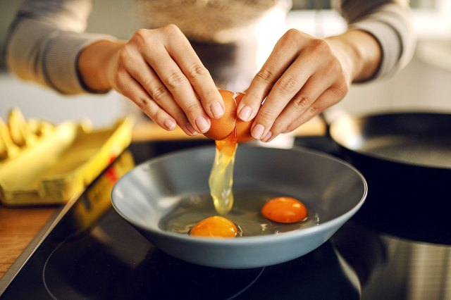 An image of a person cracking eggs into a pan