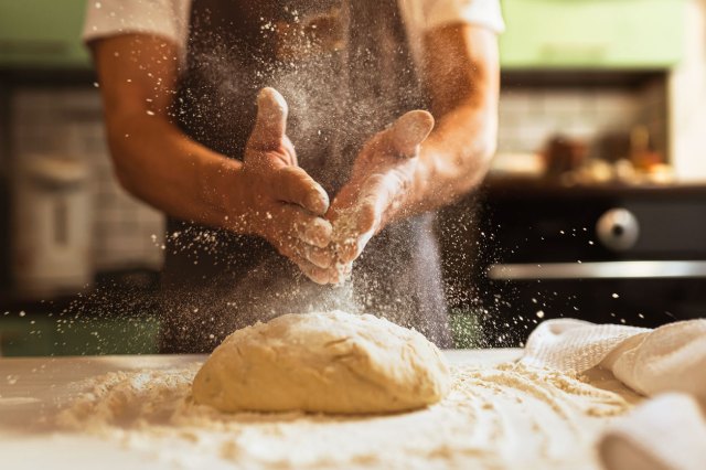 An image of a baker putting flour on his hand over bread dough