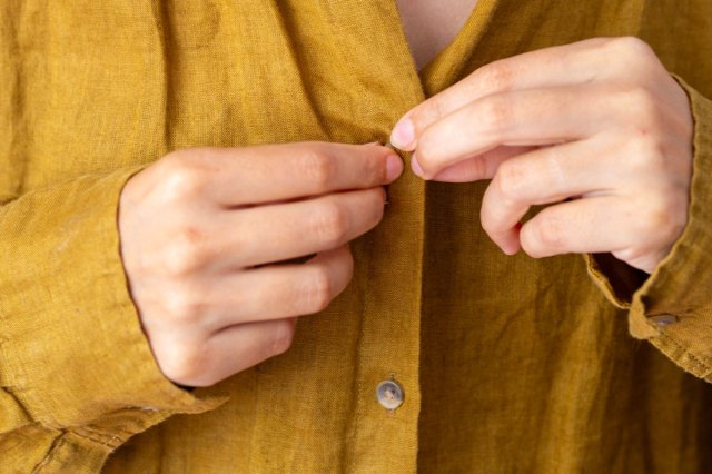 An image of person buttoning a shirt