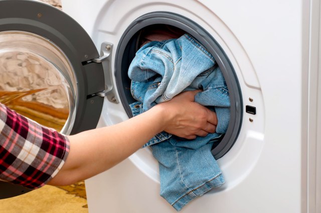 An image of a person putting a pair of jeans into the washer