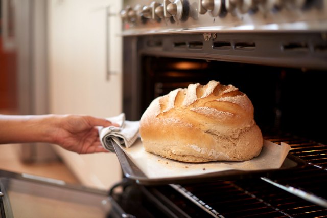 An image of a person pulling a loaf of bread out of the oven