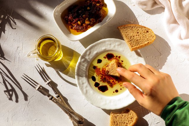 An image of a person dipping a piece of bread into a plate of oil and vinegar