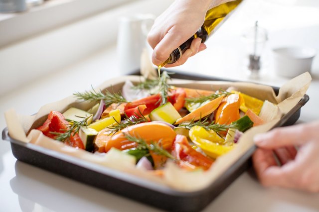 An image of oil being poured onto a baking tray of vegetables