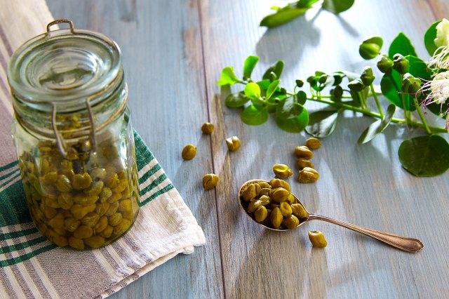 An image of a jar of capers on a wooden table