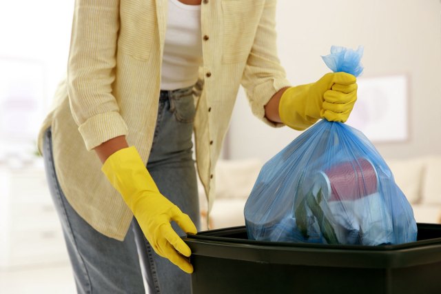 An image of a woman throwing a blue trash bag into a black trash can