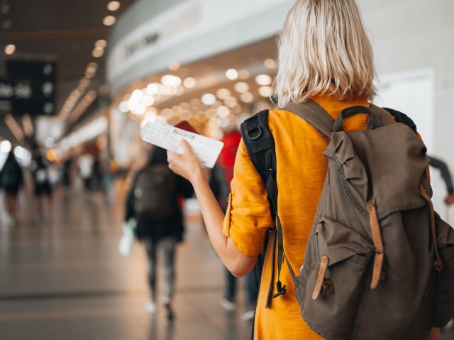 An image of a woman wearing a backpack, walking through an airport