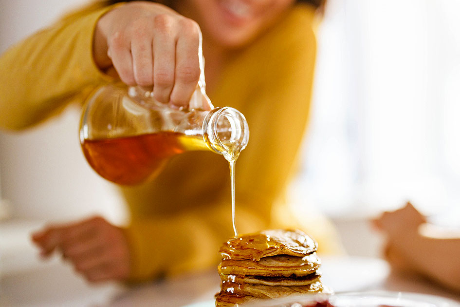 An image of a woman pouring syrup on a stack of pancakes