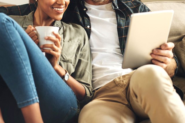 An image of a woman and a man sitting on the couch looking at a tablet
