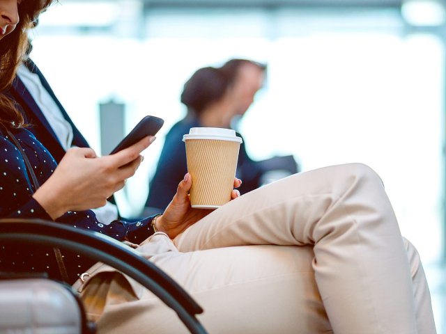 An image of a woman looking at her phone and holding a to-go cup of coffee