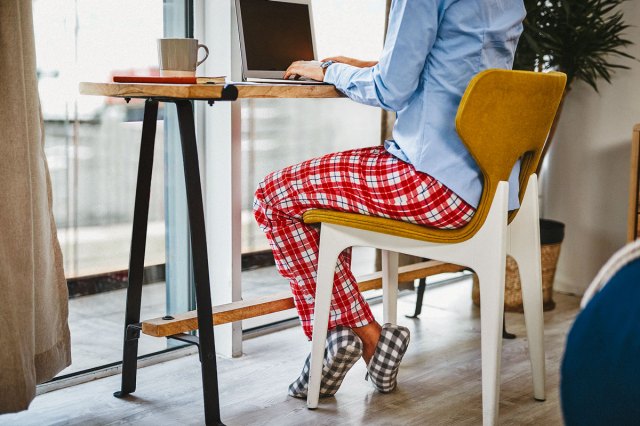 An image of a woman in plaid pajama pants sitting at a desk with a computer