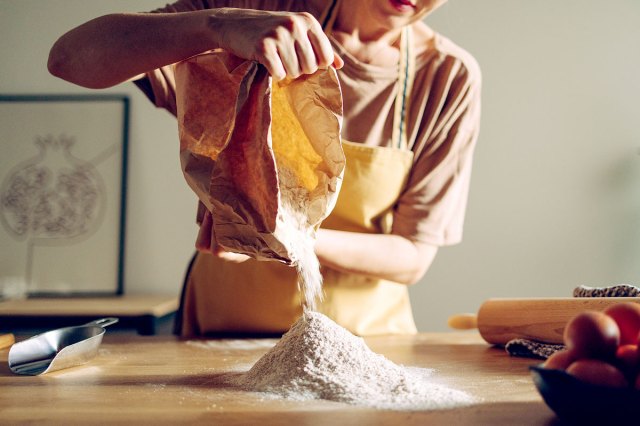 An image of a woman pouring flour onto a wooden counter