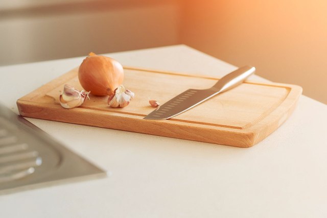 An image of an onion and a knife on a wooden cutting board