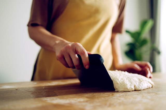 An image of a baker using a bench scraper on a ball of dough