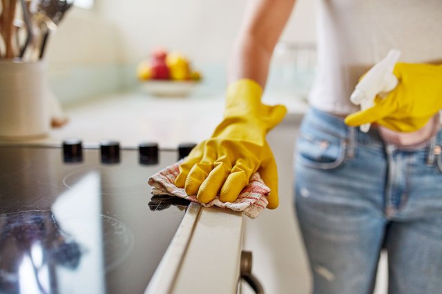 An image of a woman wearing yellow gloves cleaning the oven