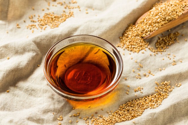 An image of a small bowl of oil on a cloth with piles of sesame seeds