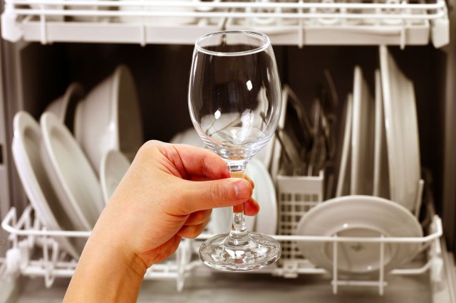 An image of a person holding a wine glass in front of a filled dishwasher