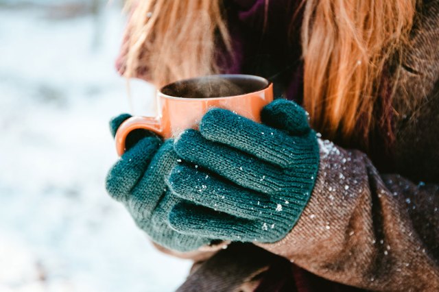 An image of a woman wearing gloves holding a steaming mug