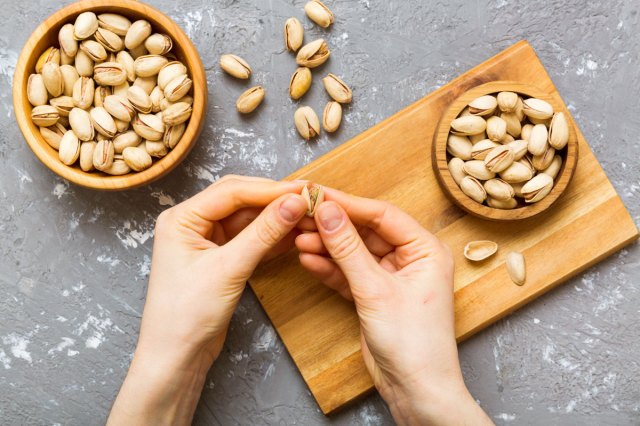 An image of a person cracking a nut open above a cutting board with a bowl of nuts