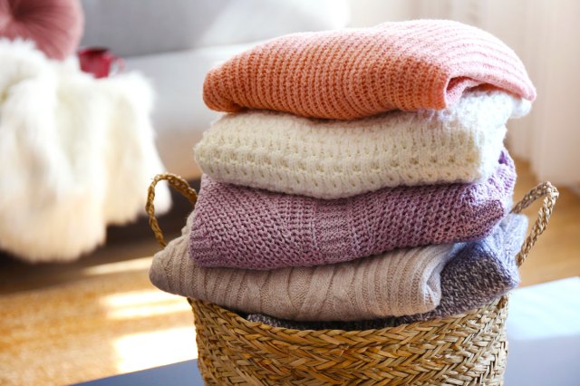 An image of folded sweaters in a wicker laundry basket