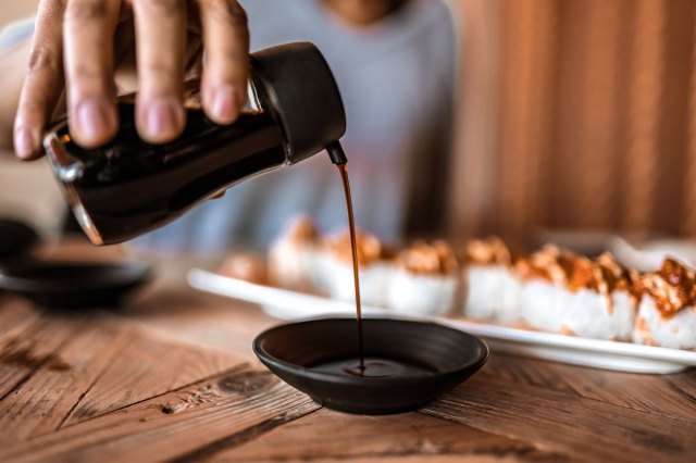 An image of a person pouring soy sauce into a small black bowl