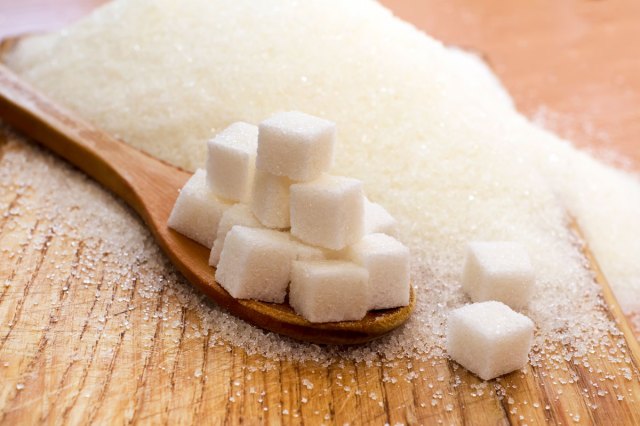 An image of sugar cubes on a wooden spoon surrounded by sugar