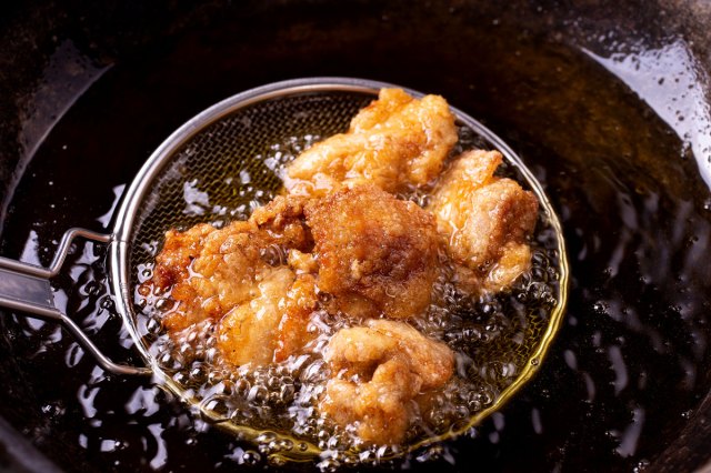 An image of fried food being taken out of a cast-iron skillet of oil