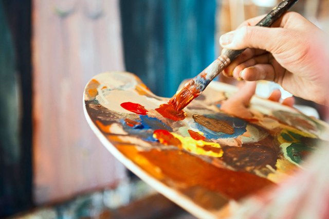 An image of a hand dipping a paintbrush into a palette 