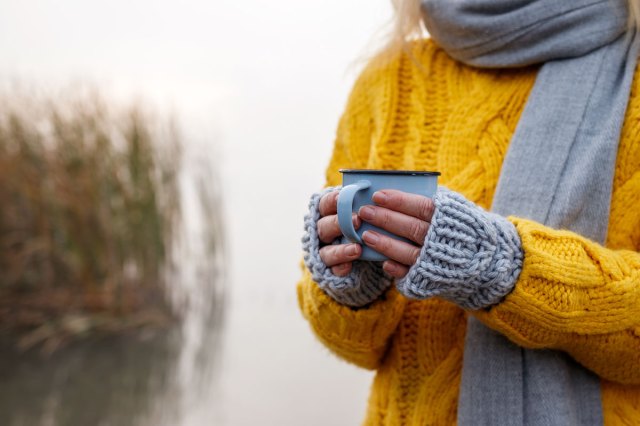 An image of a woman in sweater and scarf holding a coffee mug