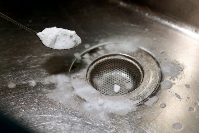 An image of baking soda being spooned into a kitchen drain