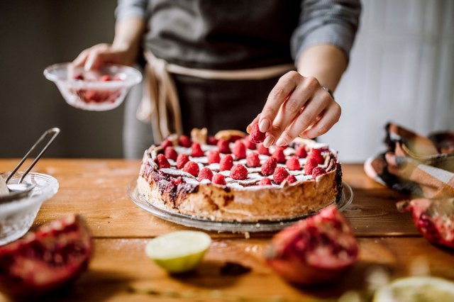 An image of a person topping a cake with raspberries