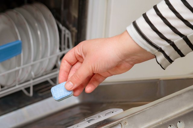 An image of a person putting a cleaning tab into a dishwasher