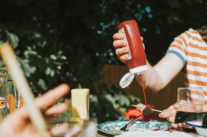 Person squirting a bottle of ketchup on a piece of meat on a stick