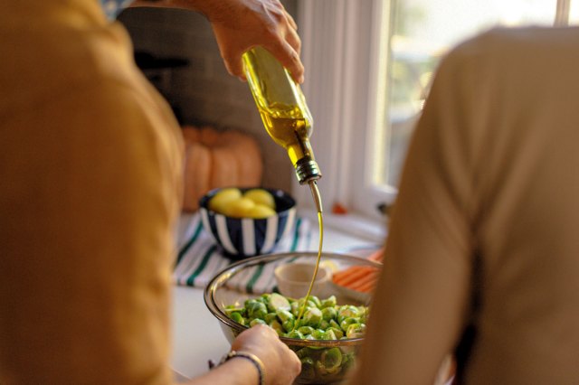An image of a person pouring oil into a bowl of vegetables