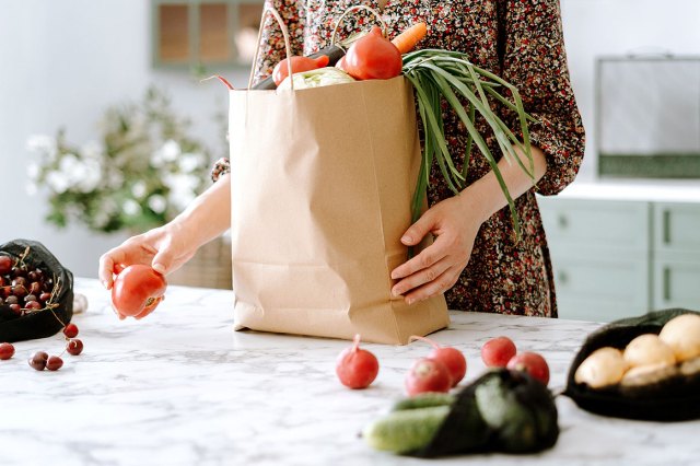 An image of a woman unpacking vegetables from paper grocery bag