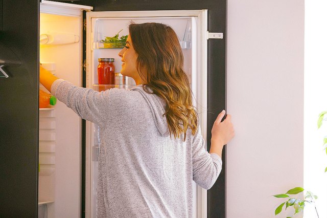 An image of a woman reaching inside the fridge