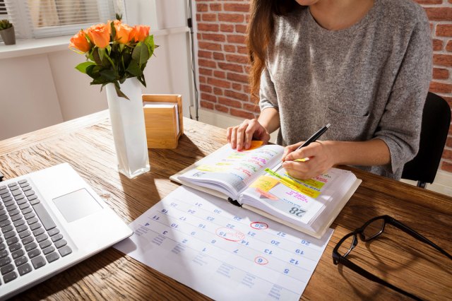An image of a woman sitting at a desk and writing in her planner