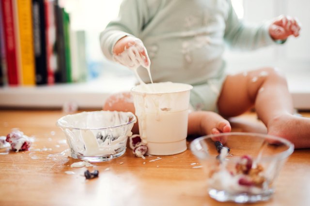 An image of a messy toddler boy sitting on kitchen counter at home, eating