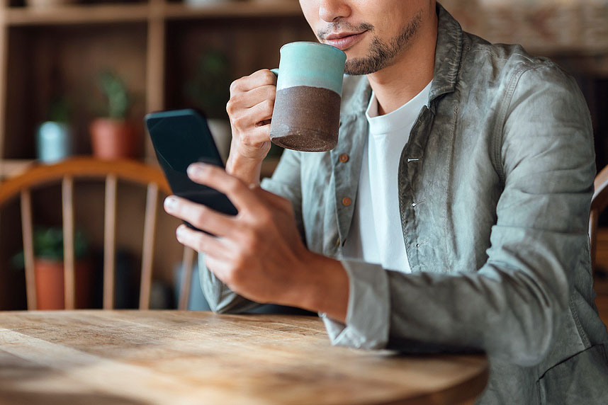An image of a man drinking a cup of coffee and looking at his phone
