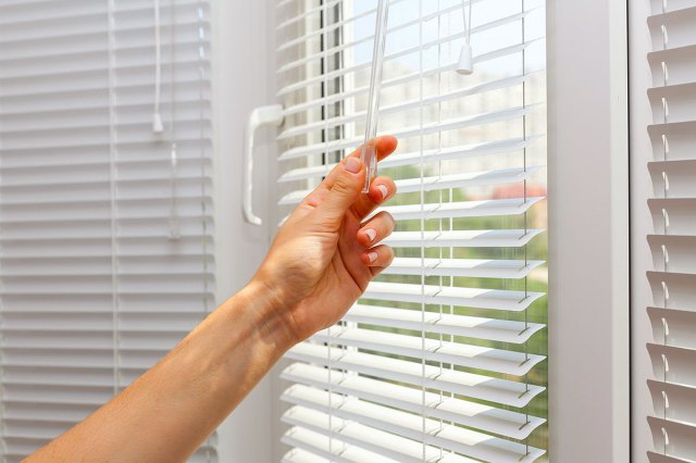 An image of a hand closing white blinds