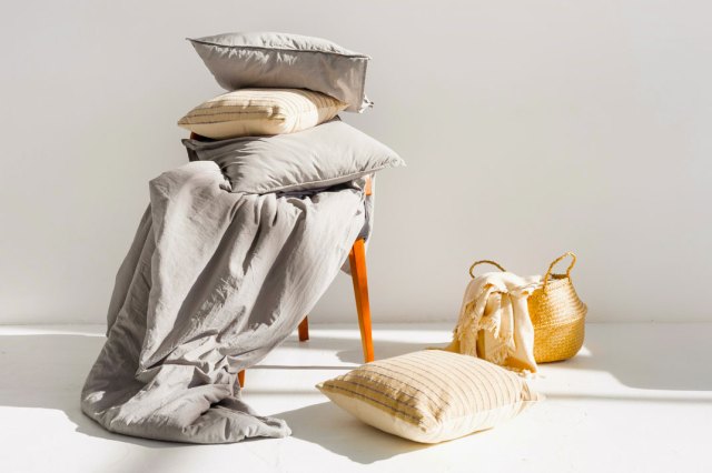 An image of bedding on a chair with a wicker basket and a pillow on the floor