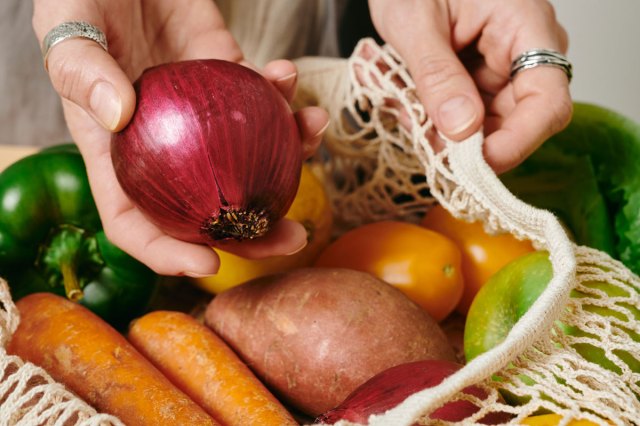 An image of a person taking a red onion out of a knit bag of vegetables