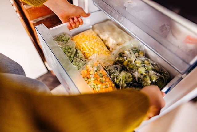 An image of a person opening a freezer filled with vegetables