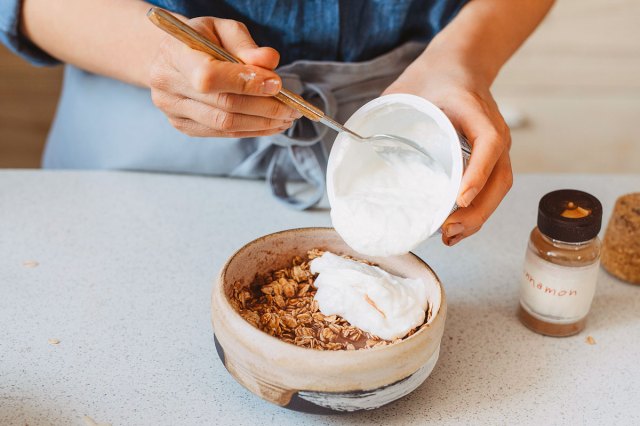 An image of a person putting yogurt into a bowl of granola