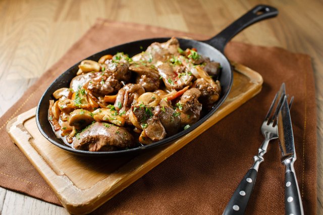 An image of liver and vegetables in a skillet on a wood cutting board